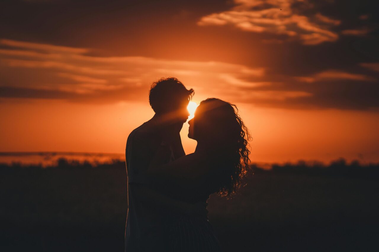 a couple kissing in front of a sunset